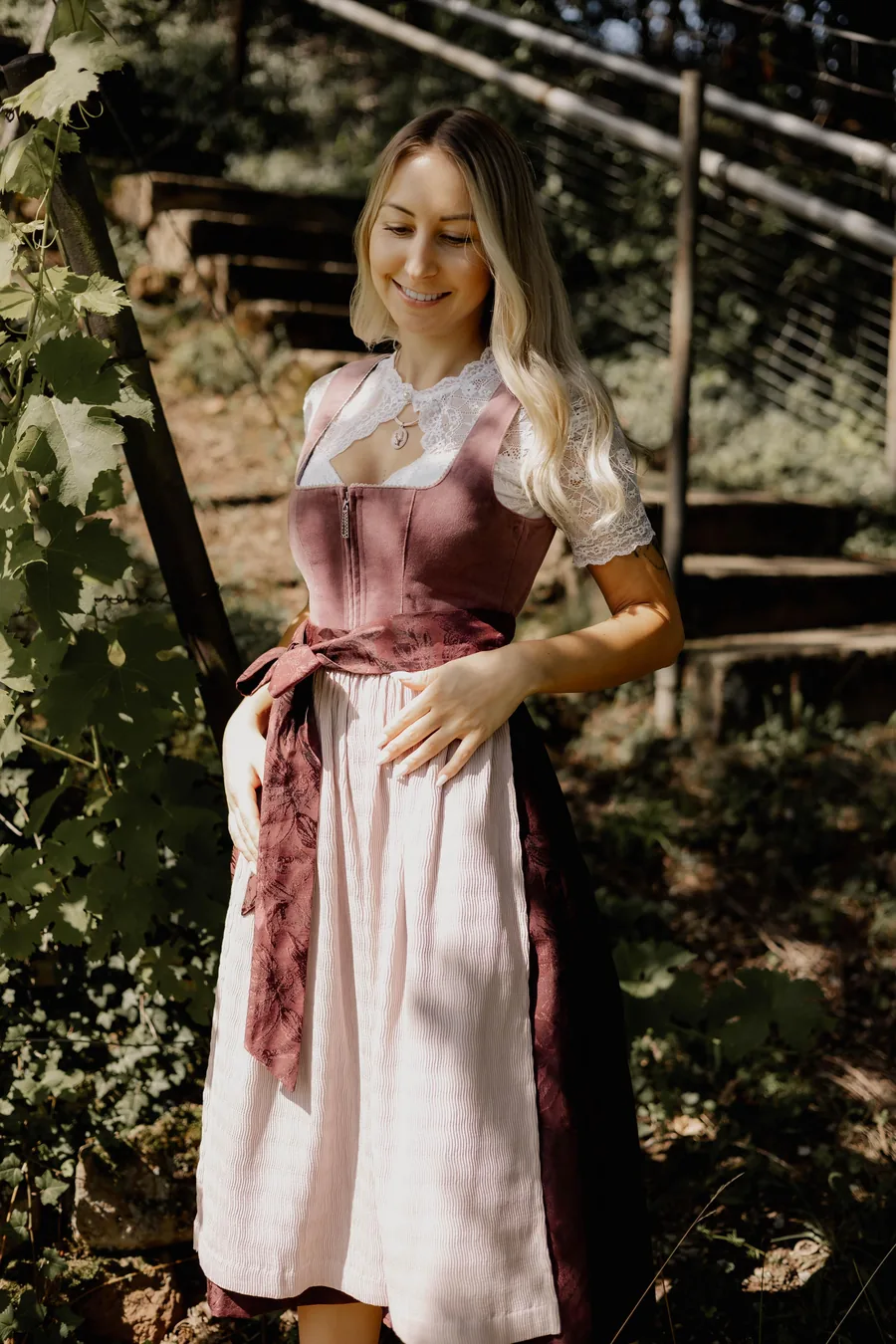 Frau im altrosa Samt-Dirndl mit rosa Schürze und weißer Spitzenbluse im Garten