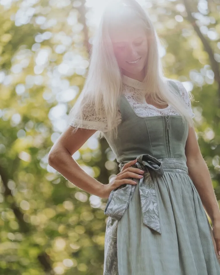 Frau in einem hellgrünen Sommer-Dirndl unter Bäumen im Gegenlicht