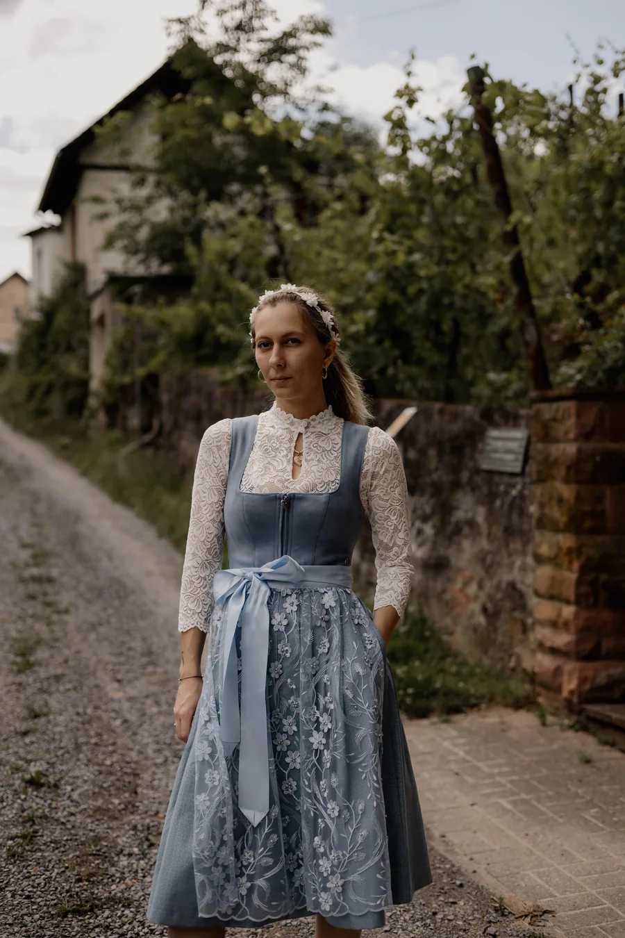 Frau im hellblauen Dirndl mit bestickter Schürze und weißer Spitzenbluse auf einem Dorfweg