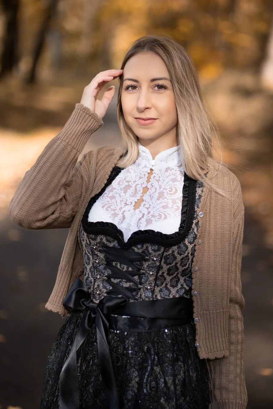 Frau im schwarzen Dirndl mit Spitzenbluse und brauner Strickjacke im herbstlichen Wald