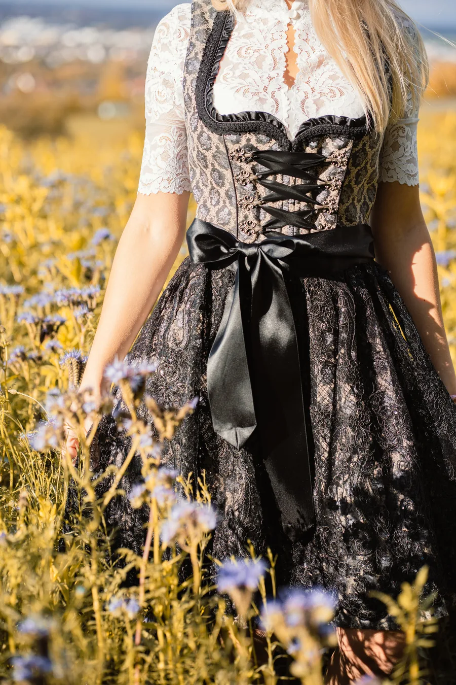 Schwarzes Dirndl mit geschnürtem Mieder und mittig gebundener Satin-Schleife auf einer Blumenwiese