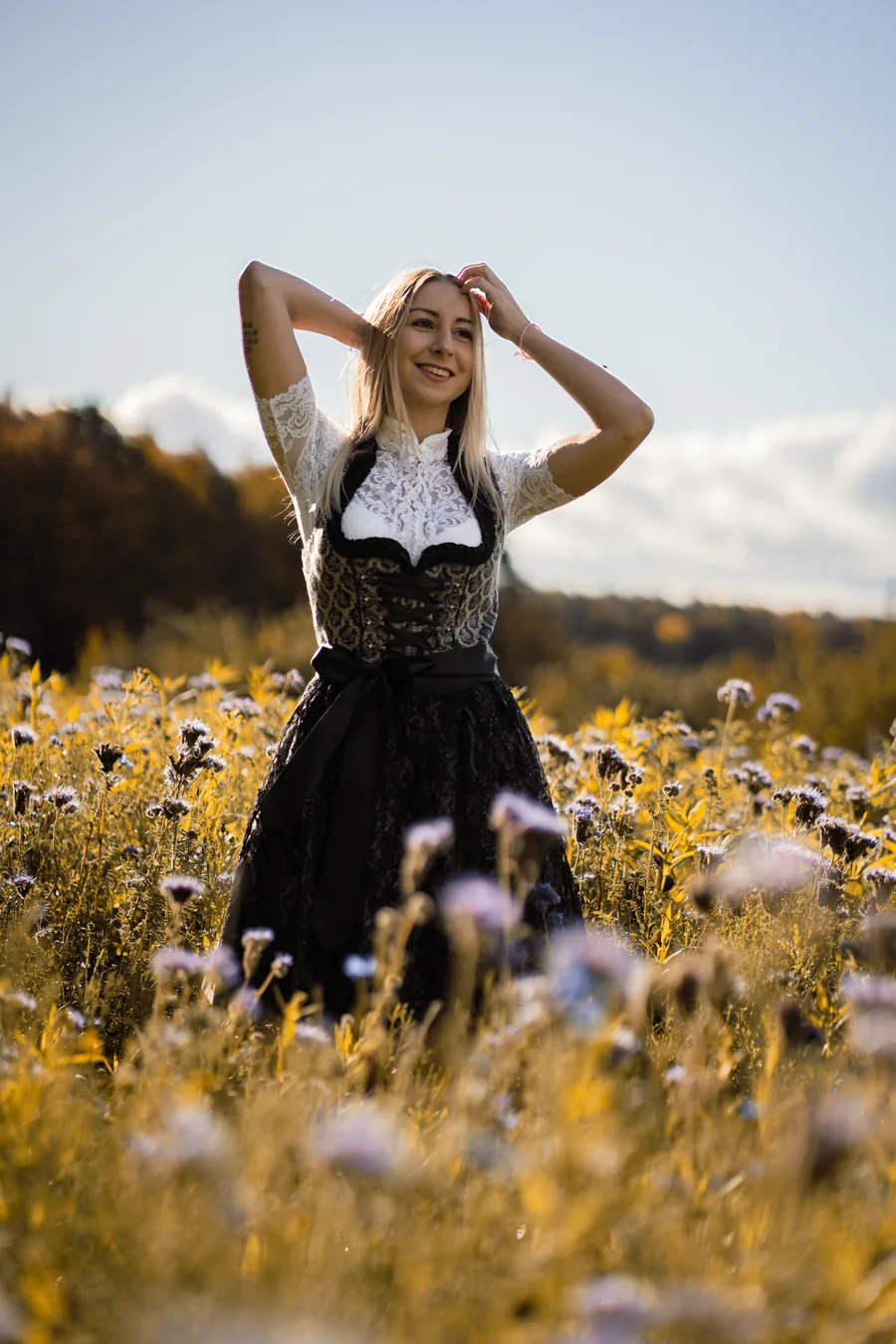 Lachende Frau im schwarzen Dirndl mit weißer Spitzenbluse auf einer Blumenwiese