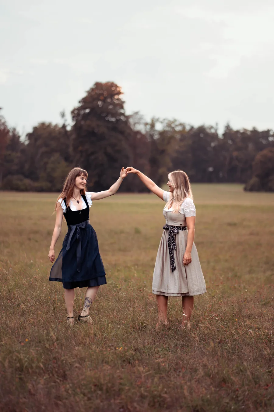 Zwei Frauen im Dirndl tanzen lachend auf einer Wiese