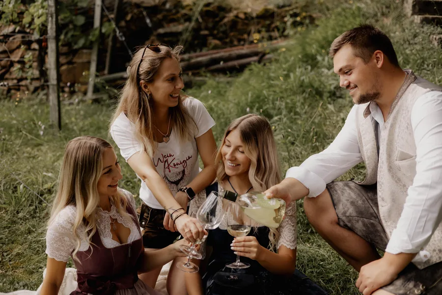 Vier junge Leute in Dirndl und Lederhosen stoßen beim Picknick mit Wein an