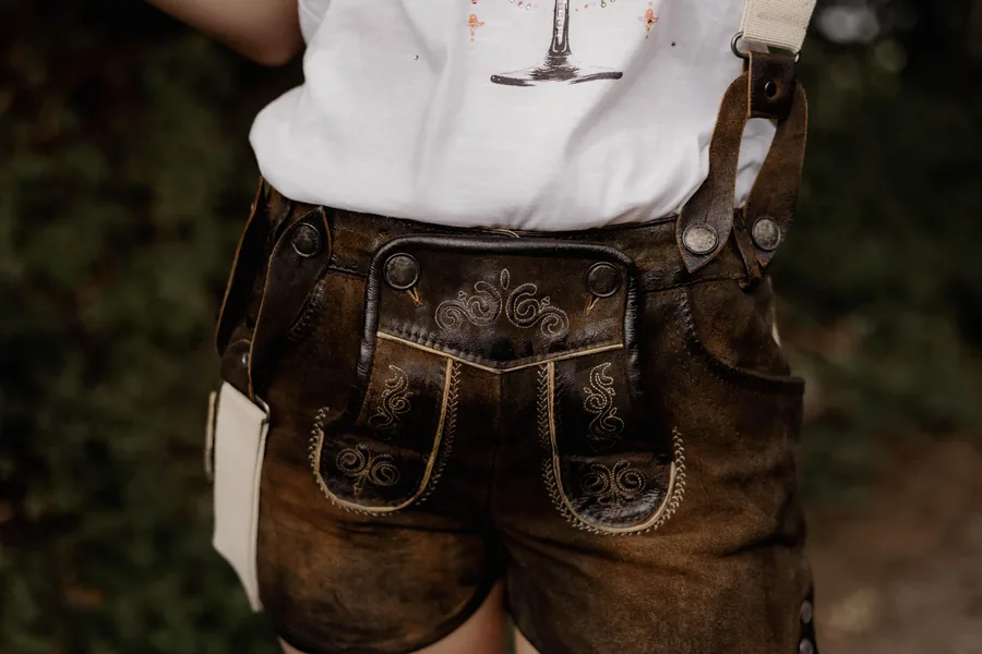 Nahaufnahme einer kurzen Lederhose von hinten: Stickerei, Hornknöpfe und helle Hosenträger